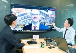 大型モニターに映る海外拠点のメンバーと打ち合わせをする社員2名